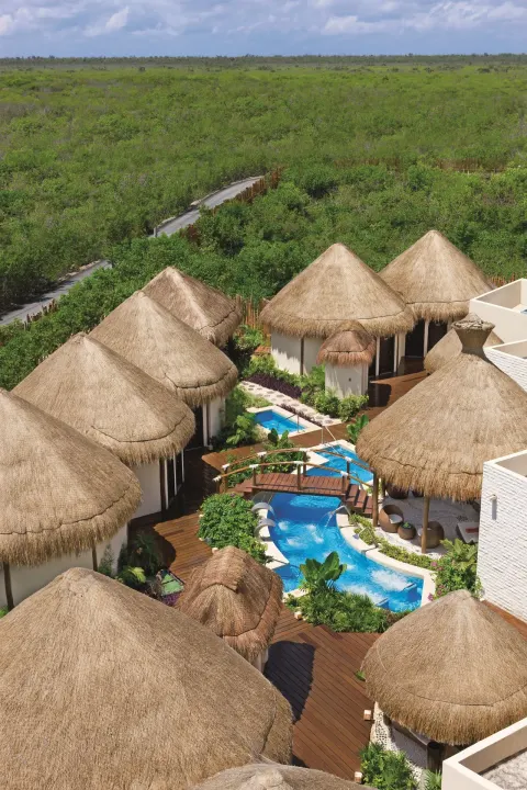 Aerial view of thatched spa buildings and winding pool at Dreams Riviera Cancun Resort & Spa.