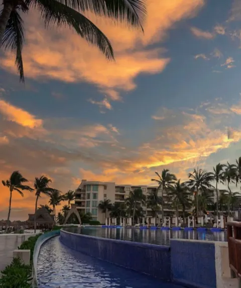 Sunset clouds glow over the pool and palms at Dreams Riviera Cancun Resort & Spa.