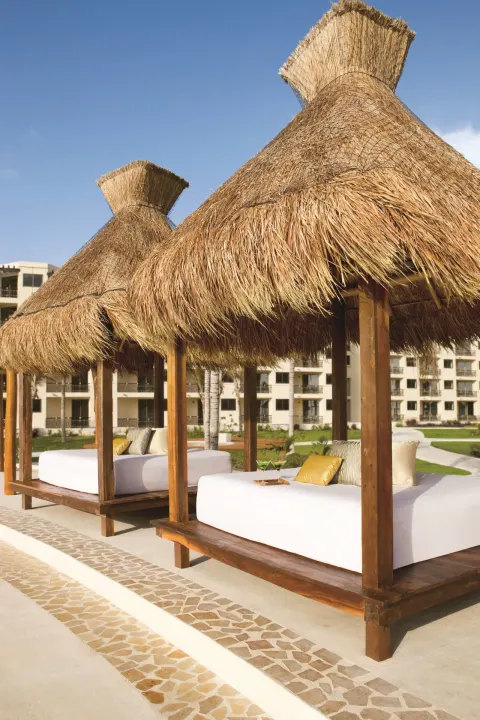 Thatched poolside daybeds line a walkway at Dreams Riviera Cancun Resort & Spa.