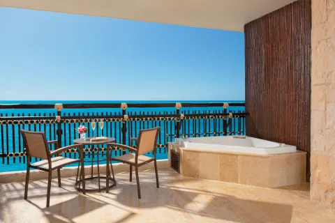 Oceanfront balcony at Dreams Riviera Cancun Resort & Spa with chairs, small table and whirlpool tub.