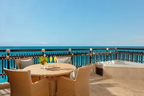 Oceanfront suite terrace at Dreams Riviera Cancun Resort & Spa with round table, chairs and whirlpool tub.