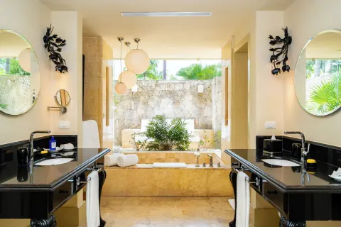 Bathroom with twin vanities, soaking tub, and outdoor stone-walled area at Eden Roc Cap Cana.