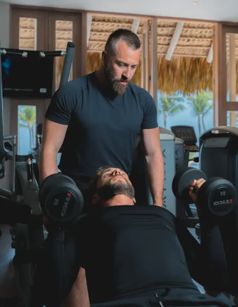 Trainer spotting a guest lifting dumbbells in the fitness center at Eden Roc Cap Cana.