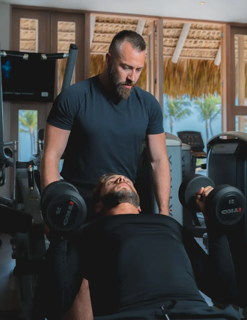 Trainer spotting a guest lifting dumbbells in the fitness center at Eden Roc Cap Cana.