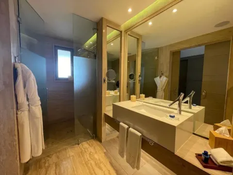 Guest bathroom with glass shower, double vanity, and bathrobes at Eden Roc Cap Cana.