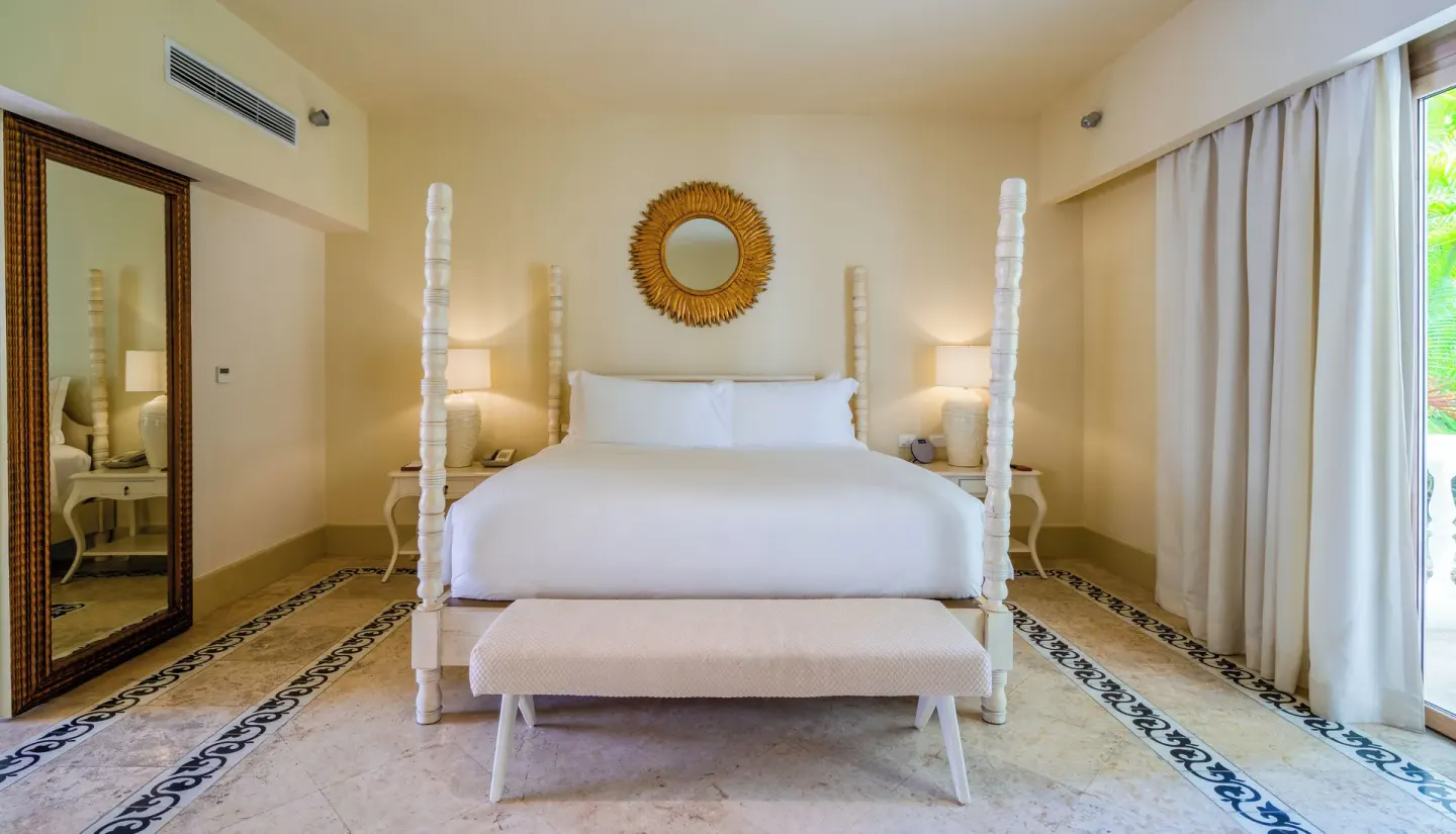Guest room with king bed, white posts, bench, and curtained terrace doors at Eden Roc Cap Cana.