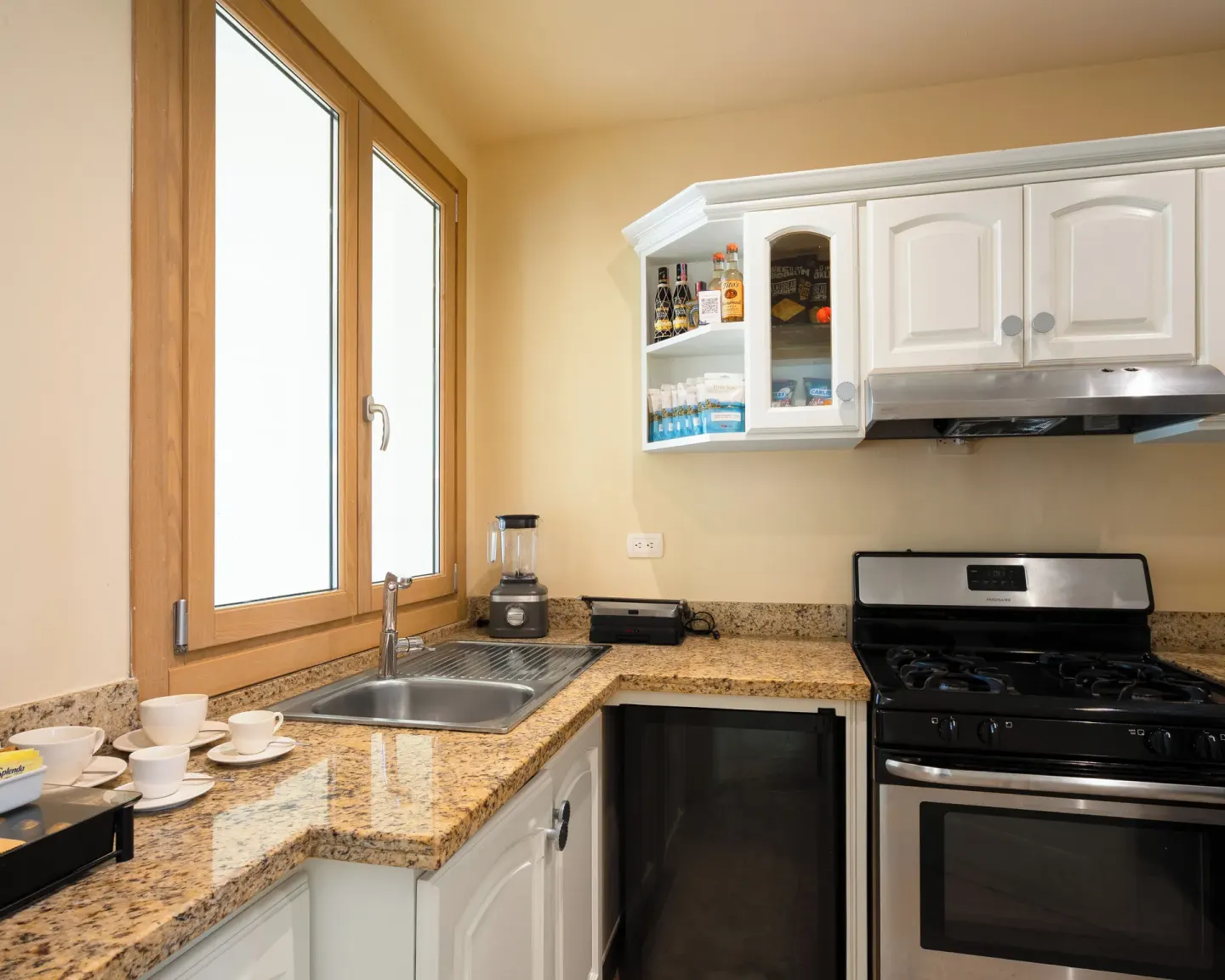 Guest-room kitchenette with sink, stove, mini fridge, and white cabinets at Eden Roc Cap Cana.