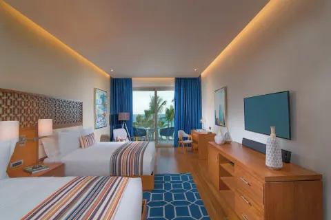 Two-bed guest room with blue curtains and balcony seating at Eden Roc Cap Cana.