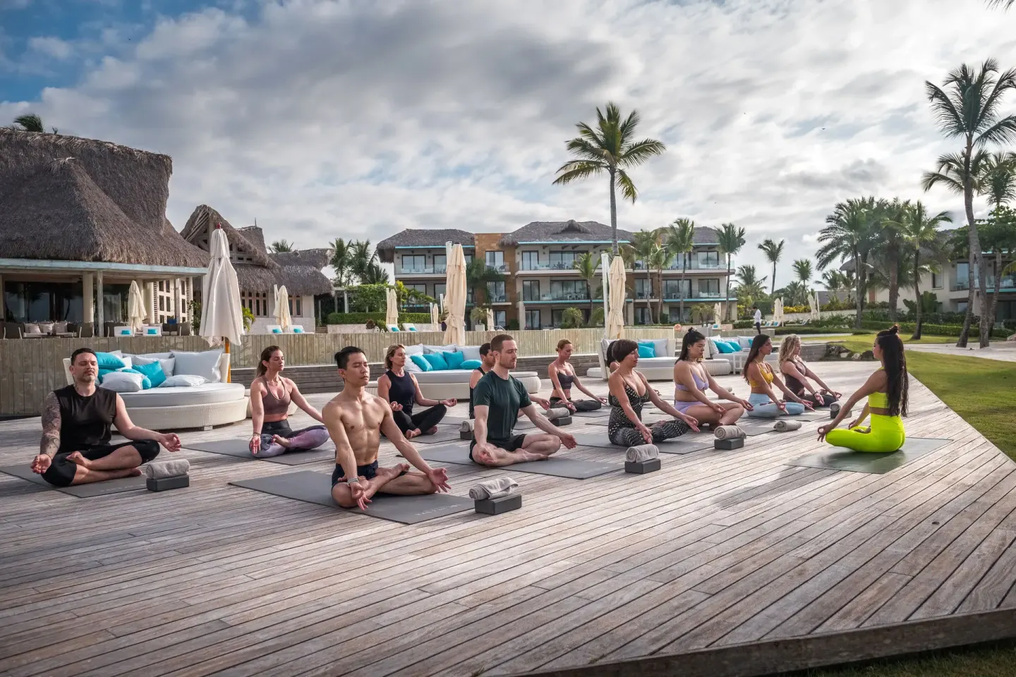 Guests meditate on yoga mats on a wooden deck at Eden Roc Cap Cana.