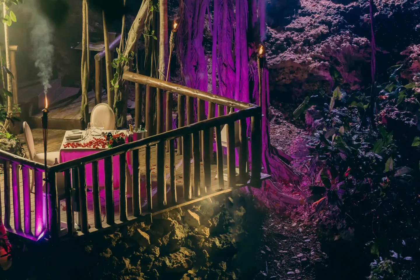 A candlelit dinner table sits on a wooden deck in a cave garden at Eden Roc Cap Cana.