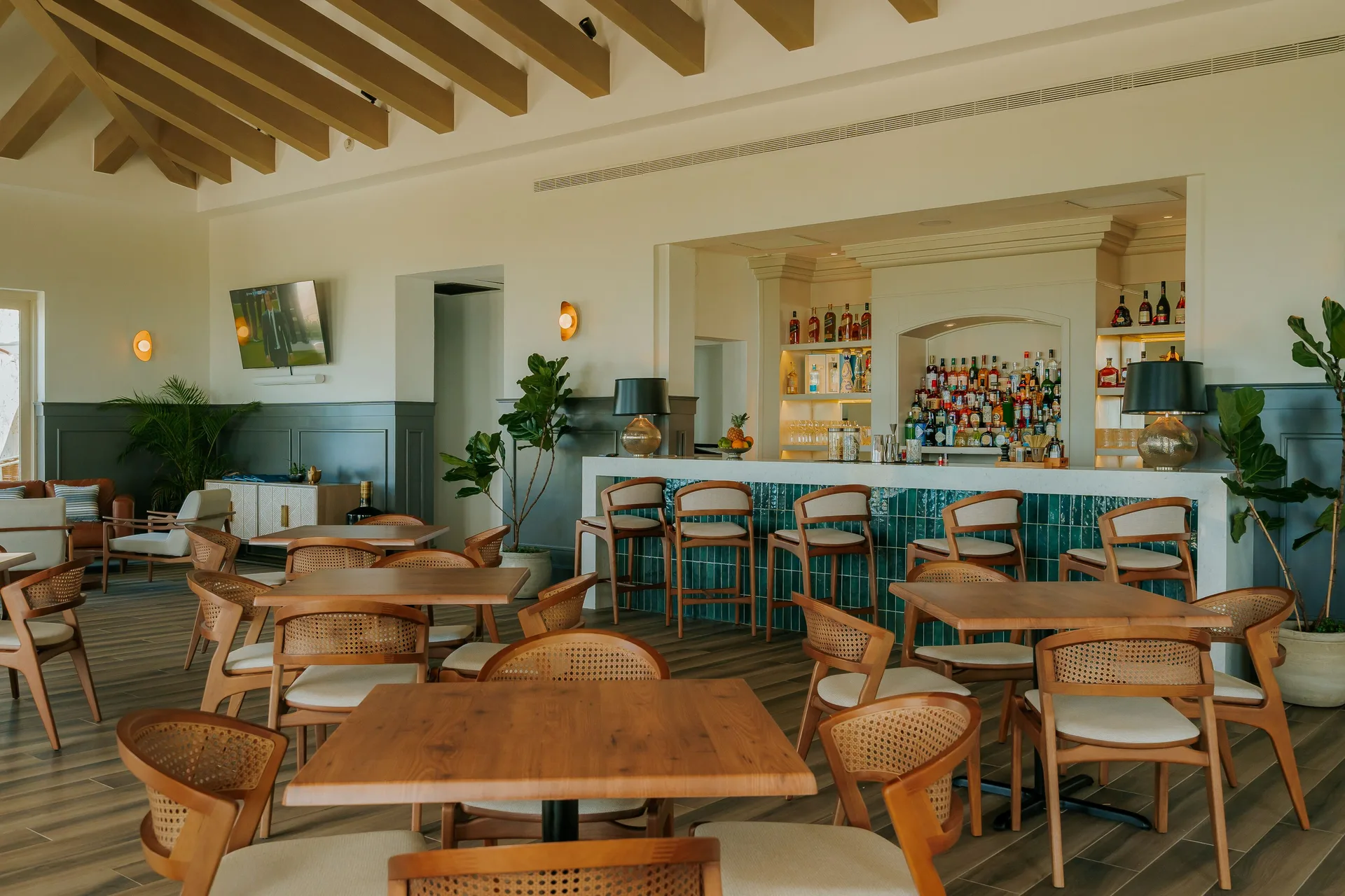 Dining room and bar at Eden Roc Cap Cana with wooden tables, cane chairs, and a tiled counter.