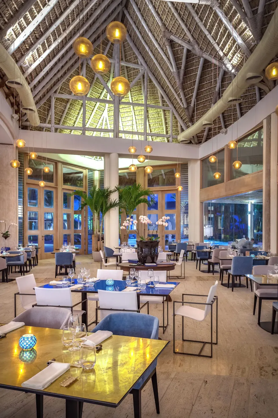 Thatched-roof dining room with set tables and pendant lights at Eden Roc Cap Cana.