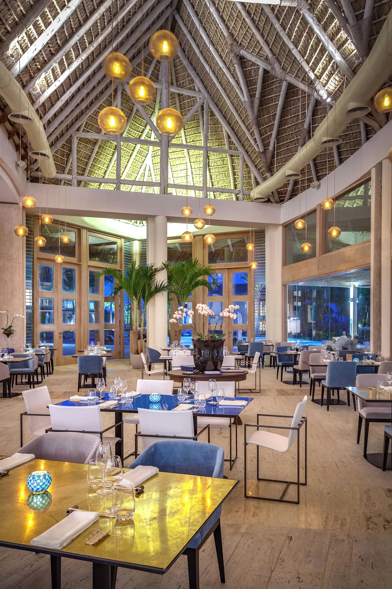 Thatched-roof dining room with set tables and pendant lights at Eden Roc Cap Cana.