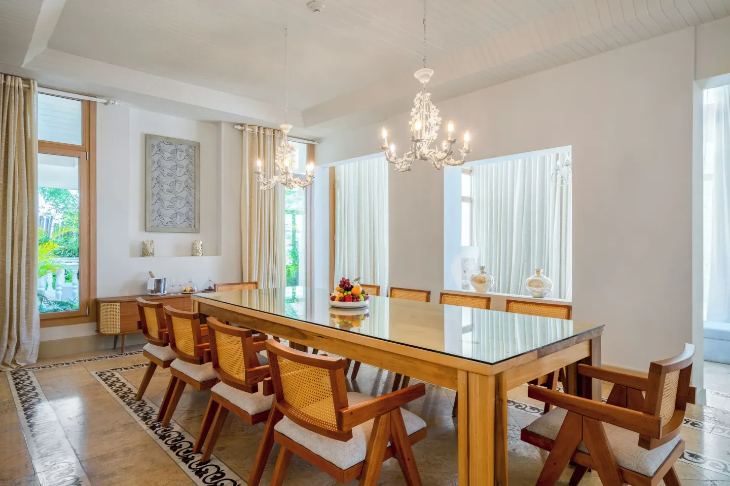 Dining room with a long table, cane chairs, and chandeliers at Eden Roc Cap Cana.