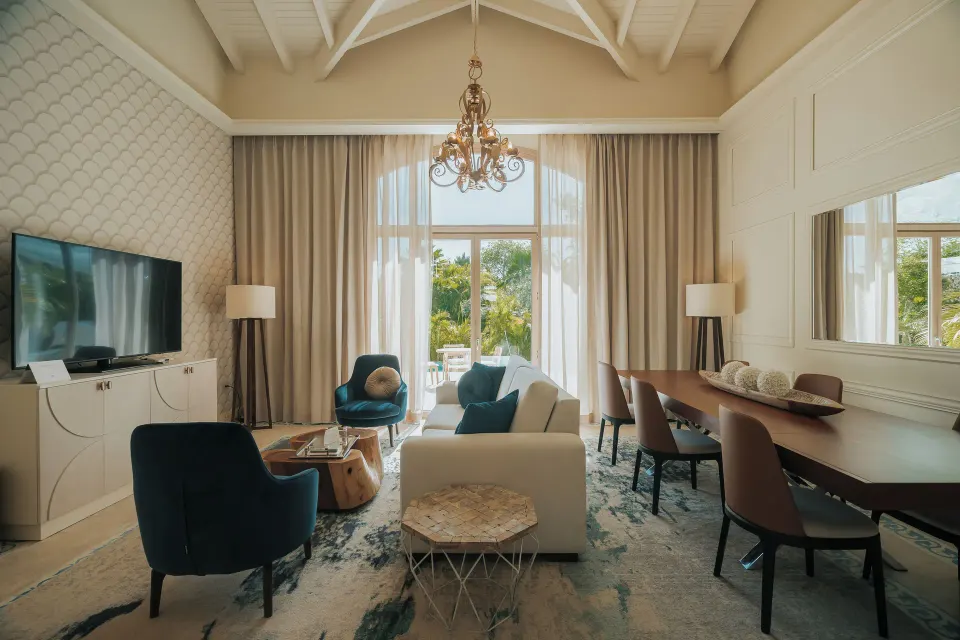 Living and dining area of a two-bedroom villa at Eden Roc Cap Cana with sofa, TV and long table.