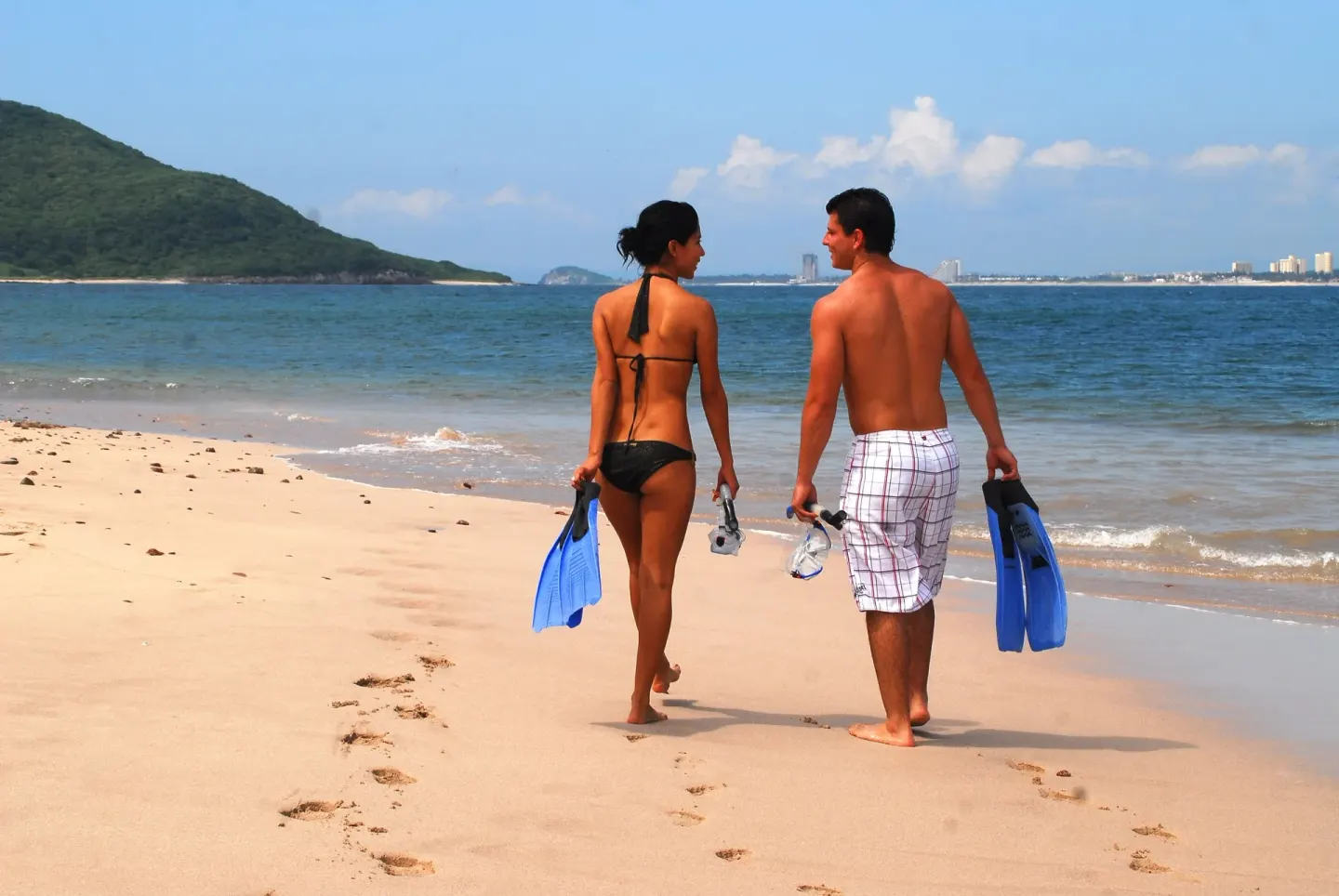 A couple carries snorkel gear while walking along the beach at El Cid Castilla Beach Hotel.