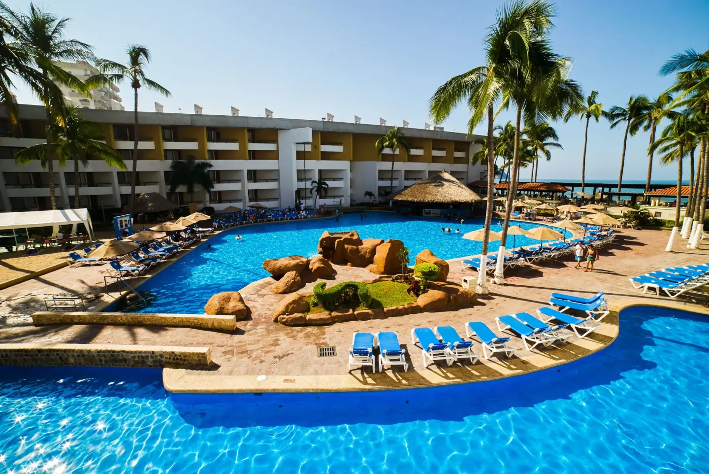 Curved resort pool with rock island and ocean beyond at El Cid Castilla Beach Hotel.