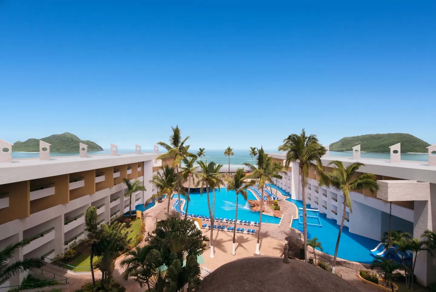 Elevated view of pool courtyard, palms, ocean, and islands at El Cid Castilla Beach Hotel.