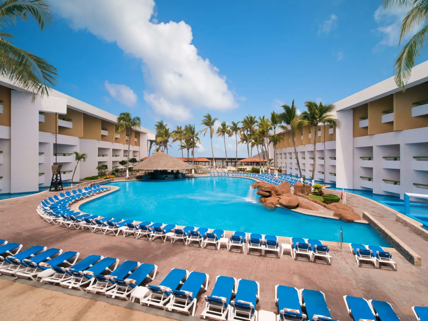 Large pool lined with blue loungers between hotel wings at El Cid Castilla Beach Hotel.