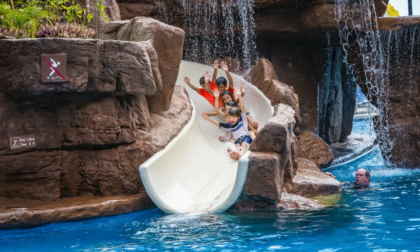 Group riding a white pool slide beneath waterfalls at El Cid Castilla Beach Hotel.