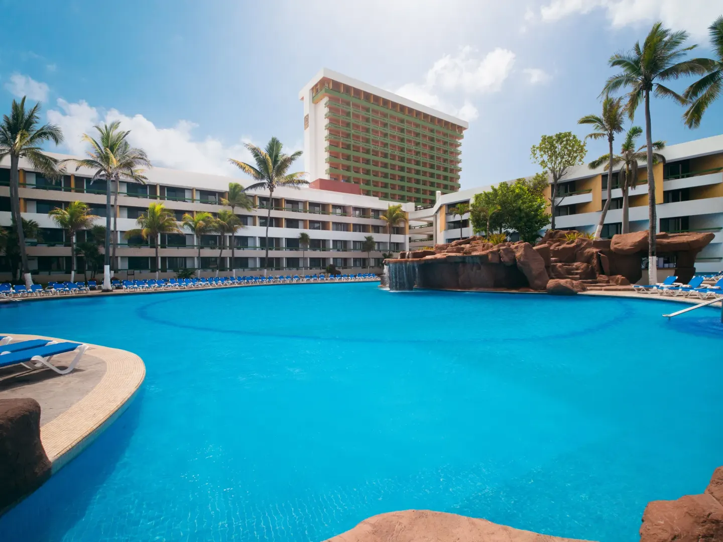 Large resort pool with lounge chairs and palm trees at El Cid Castilla Beach Hotel.