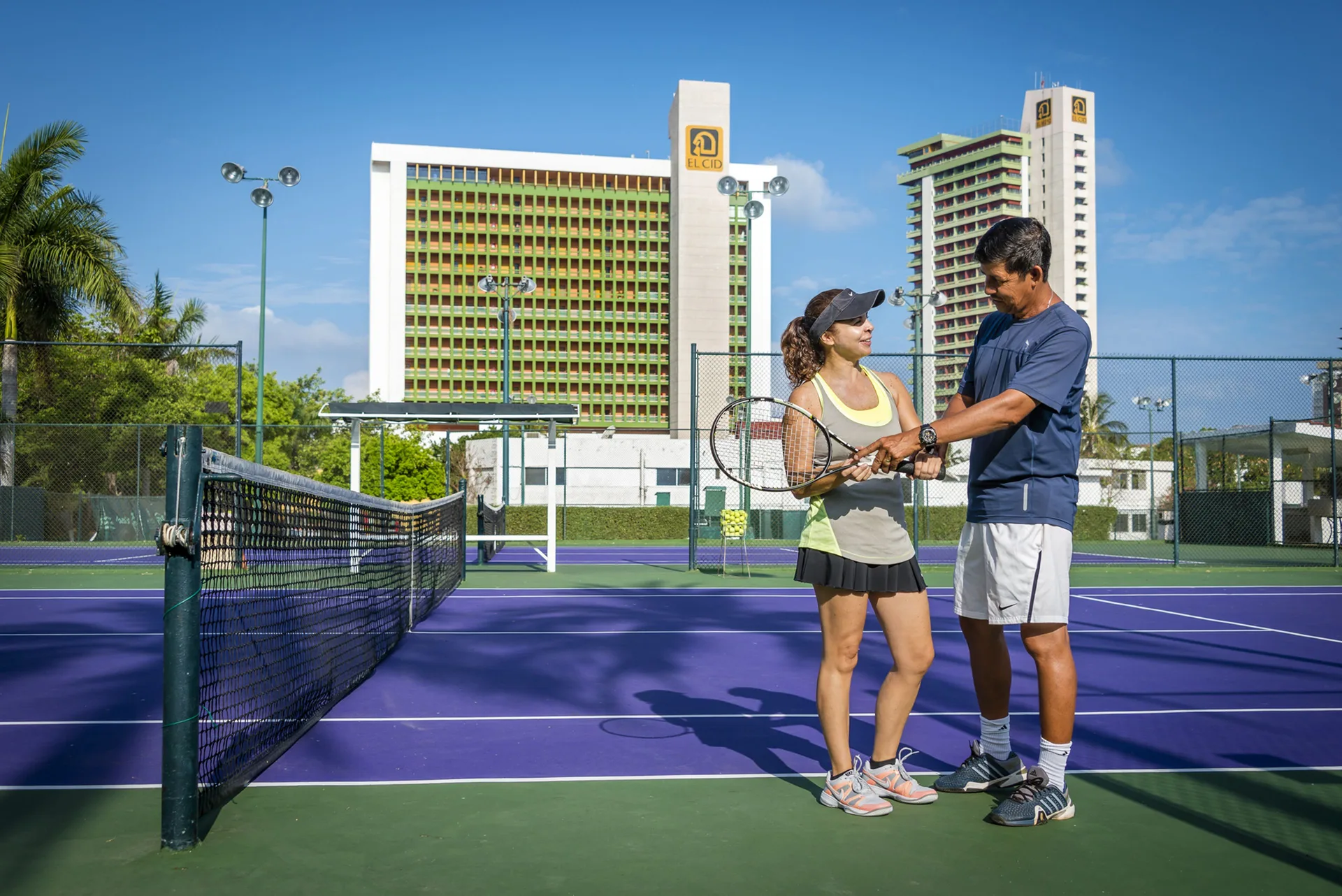 Tennis instruction on a purple court at El Cid Castilla Beach Hotel, with resort towers behind.