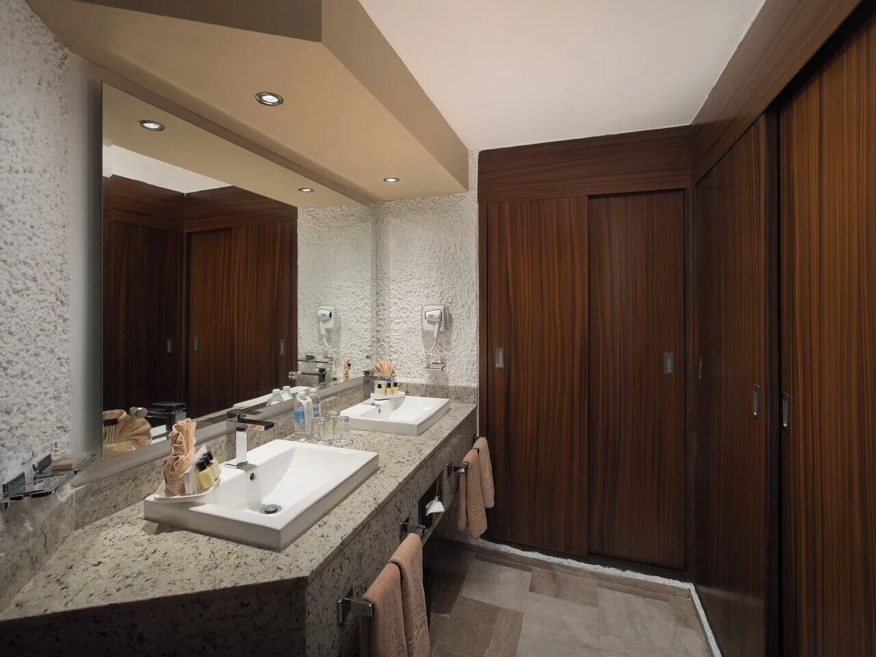 Guest bathroom with double vanity and wood closet doors at El Cid El Moro Beach Hotel.