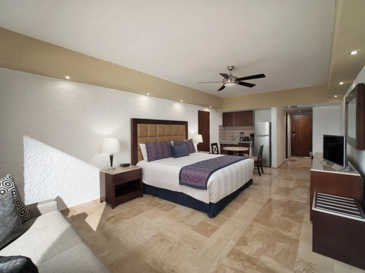 Guest room with king bed, kitchenette, TV, and seating area at El Cid El Moro Beach Hotel.