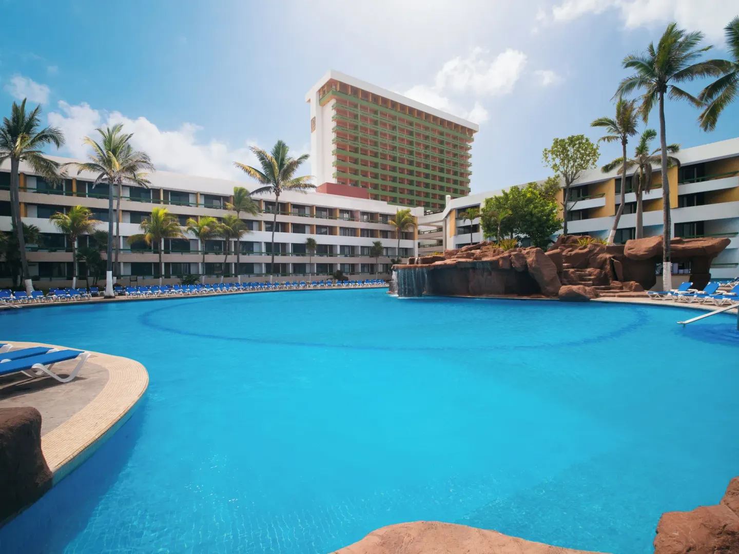 Large resort pool with palm trees and hotel towers at El Cid El Moro Beach Hotel.