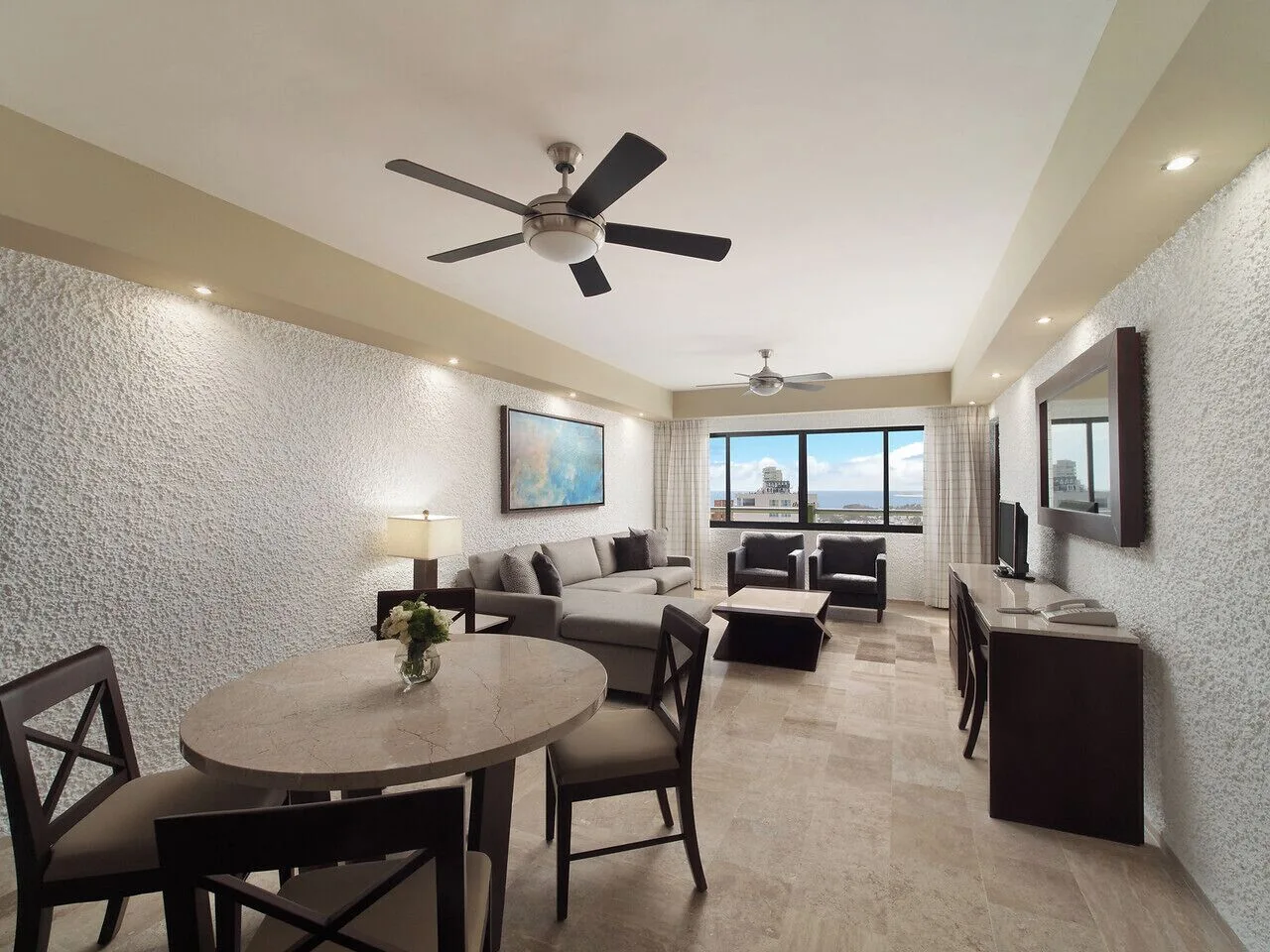 Suite living room with dining table, sofa, chairs, and window view at El Cid El Moro Beach Hotel.
