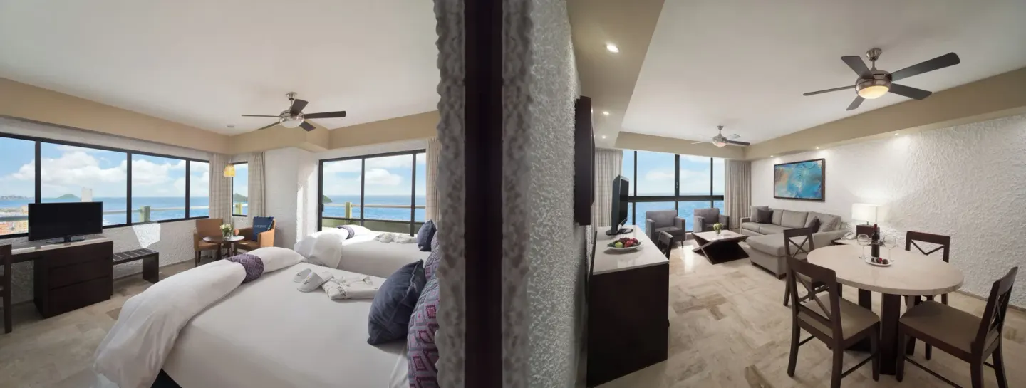 Suite layout with bedroom and living area by ocean-view windows at El Cid El Moro Beach Hotel.
