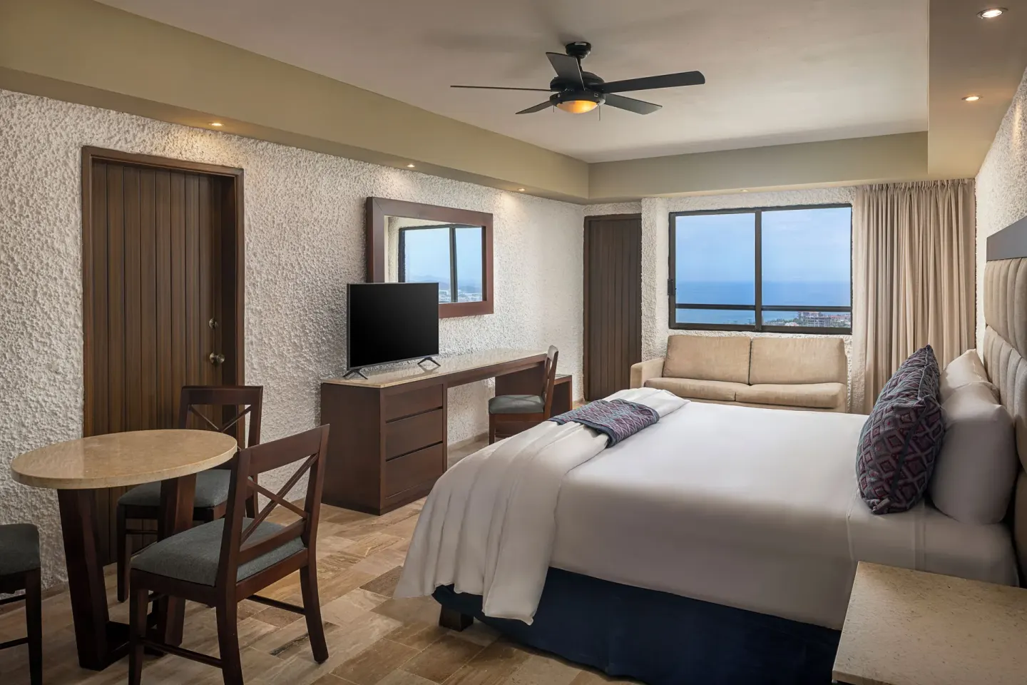 King bed guest room with sofa and ocean-facing window at El Cid El Moro Beach Hotel.