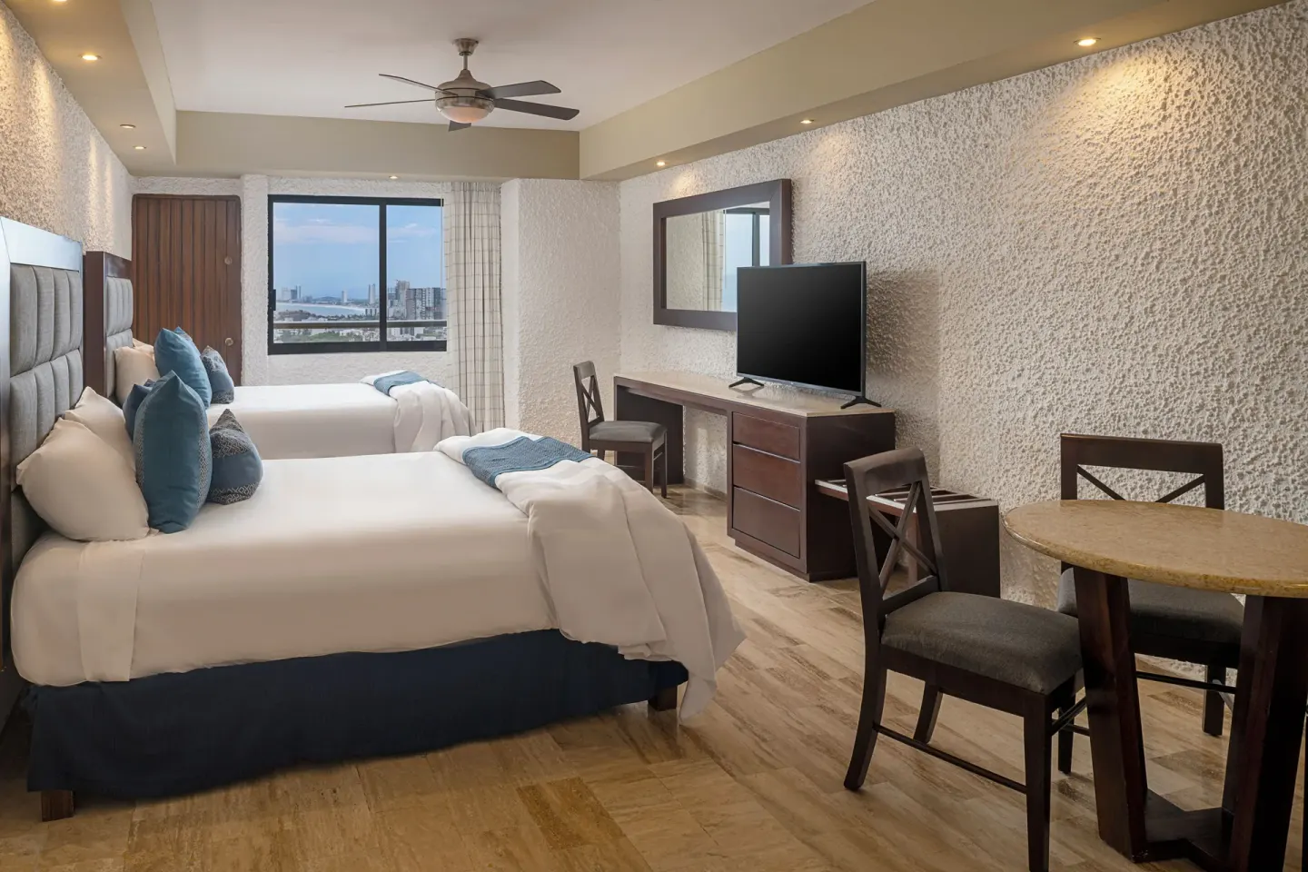 Two-bed guest room with dining table and window view at El Cid El Moro Beach Hotel.