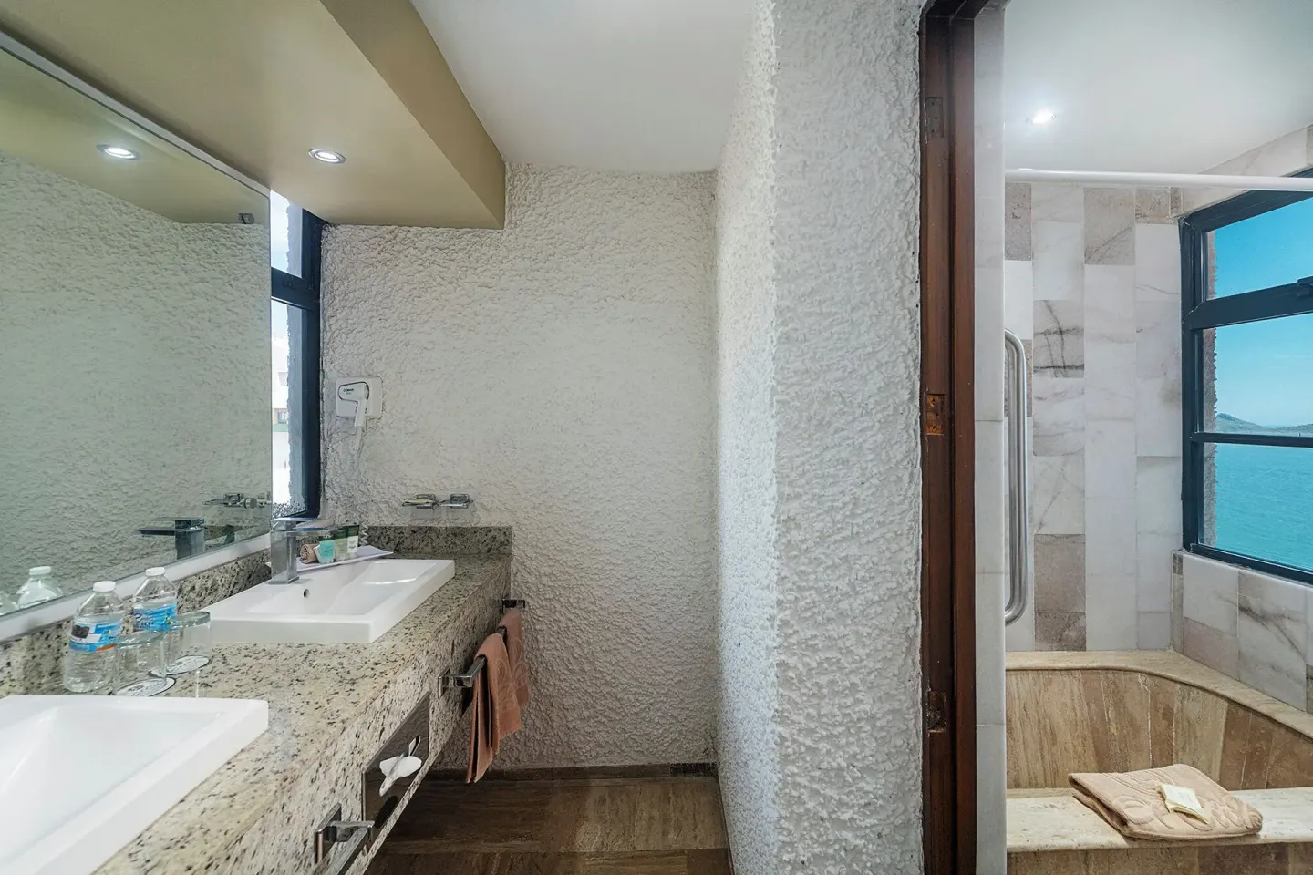One Bedroom Suite bathroom vanity and tub area with ocean-view window at El Cid El Moro Beach Hotel.