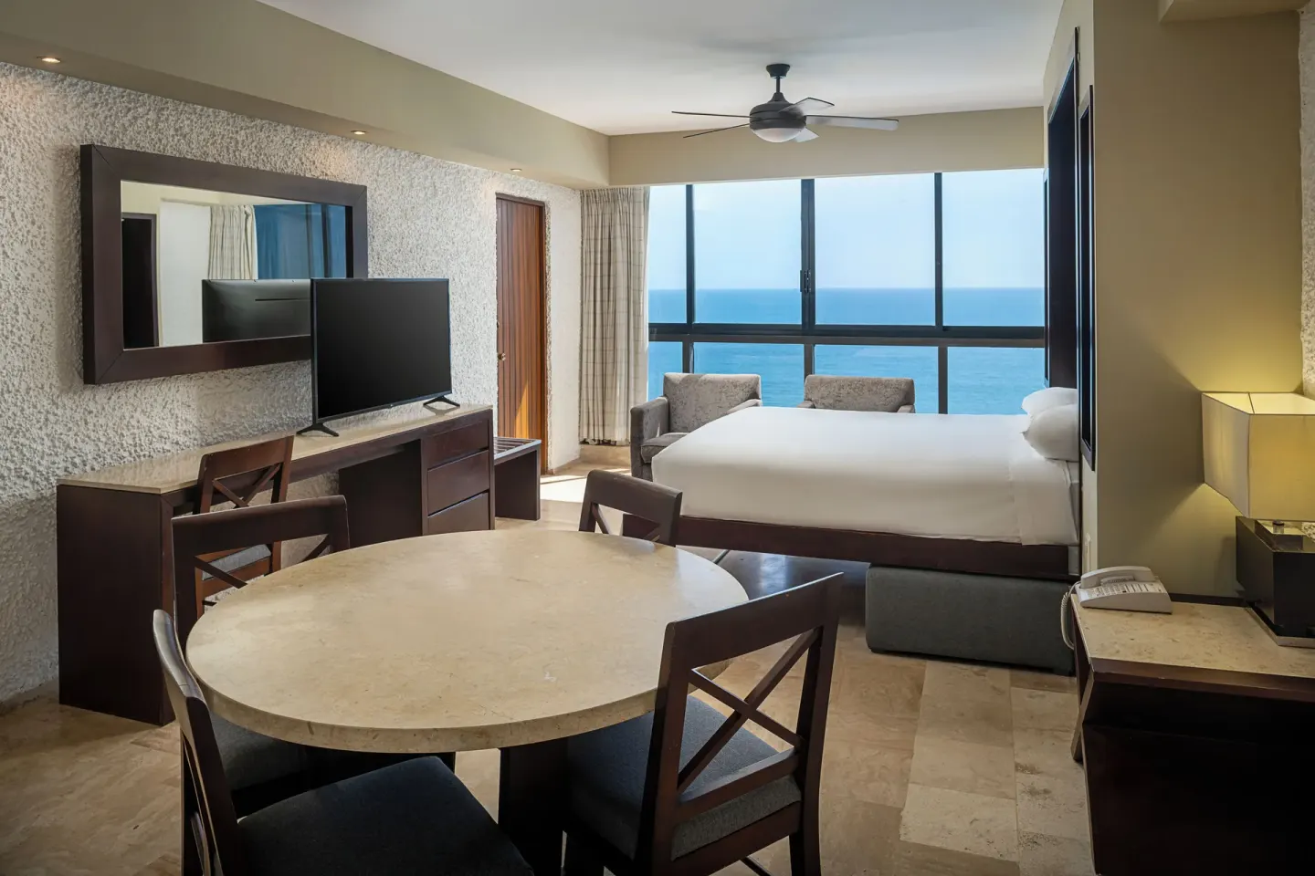 One Bedroom Suite with king bed, dining table, and ocean-facing windows at El Cid El Moro Beach Hotel.