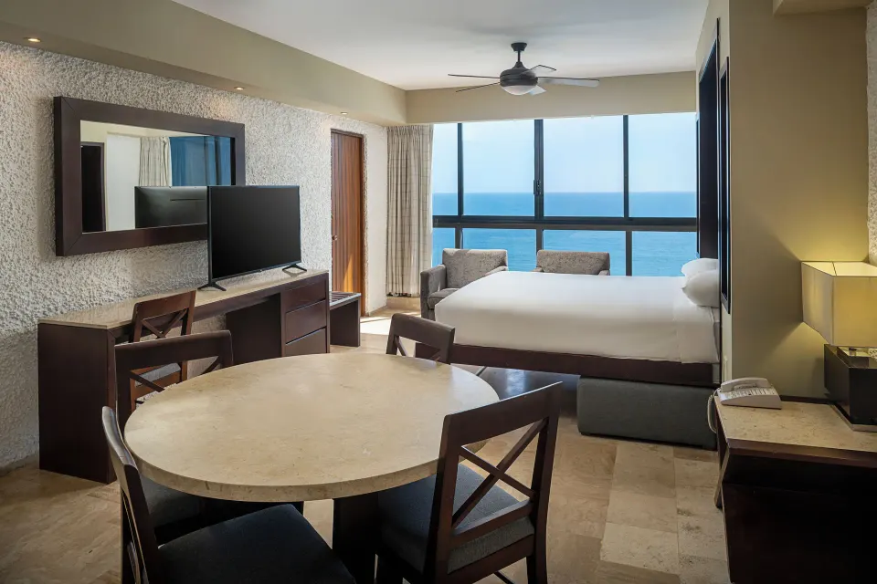 One Bedroom Suite with king bed, dining table, and ocean-facing windows at El Cid El Moro Beach Hotel.