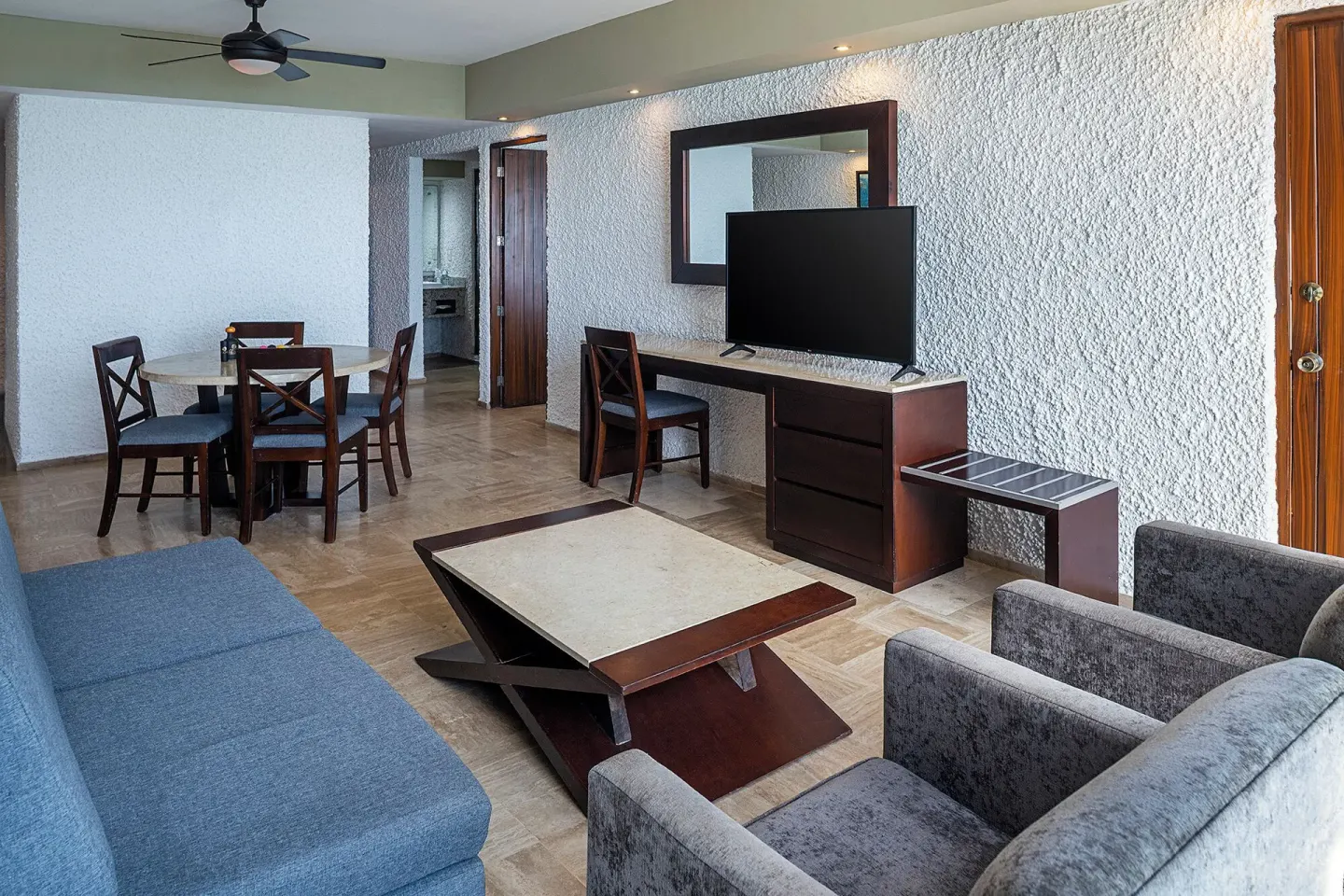 One Bedroom Suite living area with sofa, armchairs, dining table, and TV at El Cid El Moro Beach Hotel.