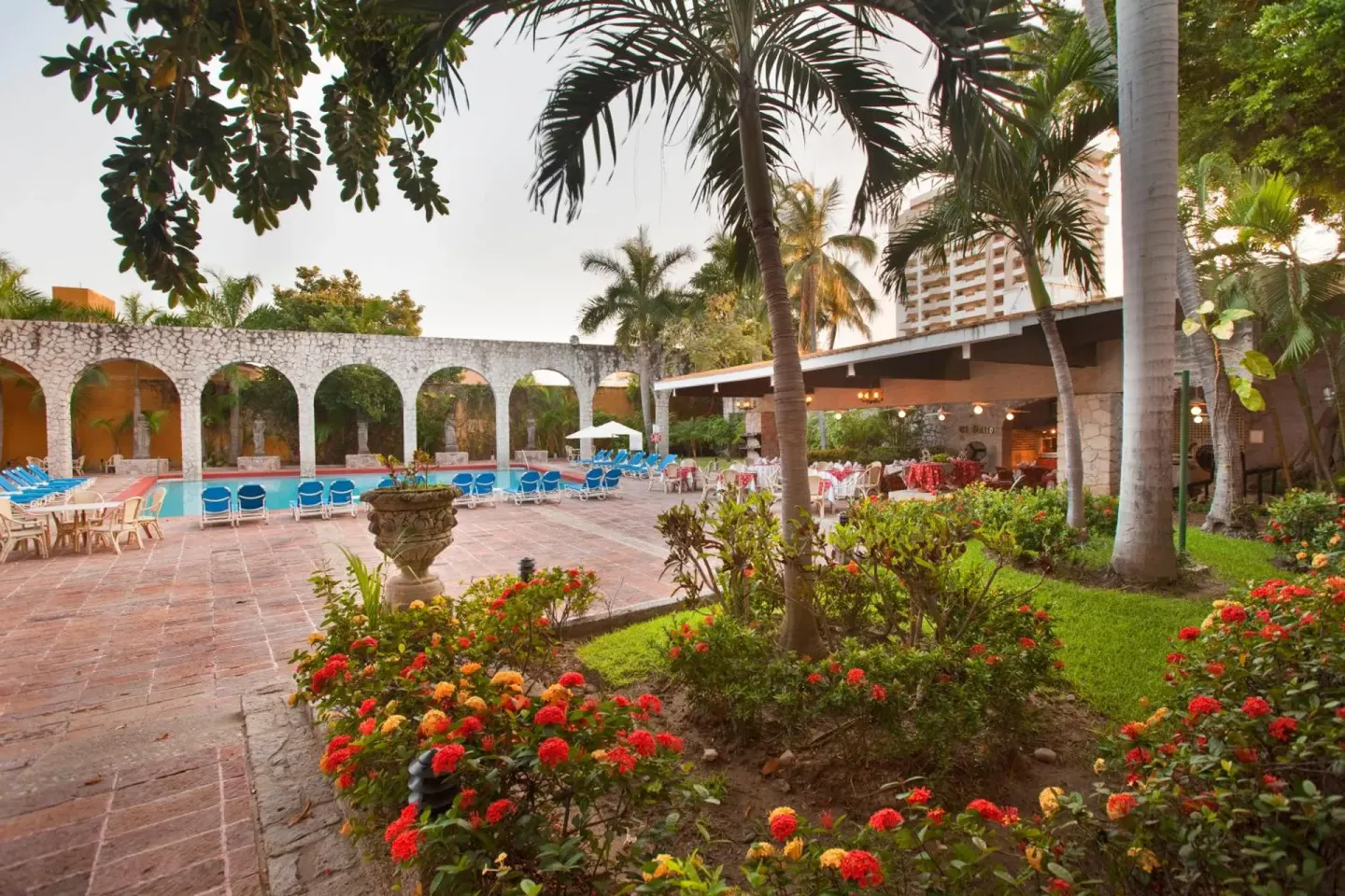 Garden courtyard with flowers, palms, pool, and terrace dining at El Cid Granada Hotel.