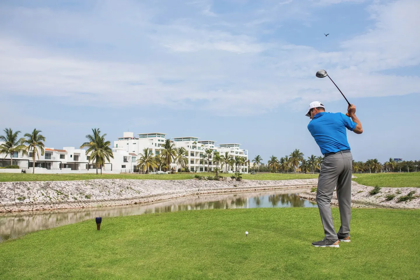 Golfer teeing off across a water feature near El Cid Granada Hotel.