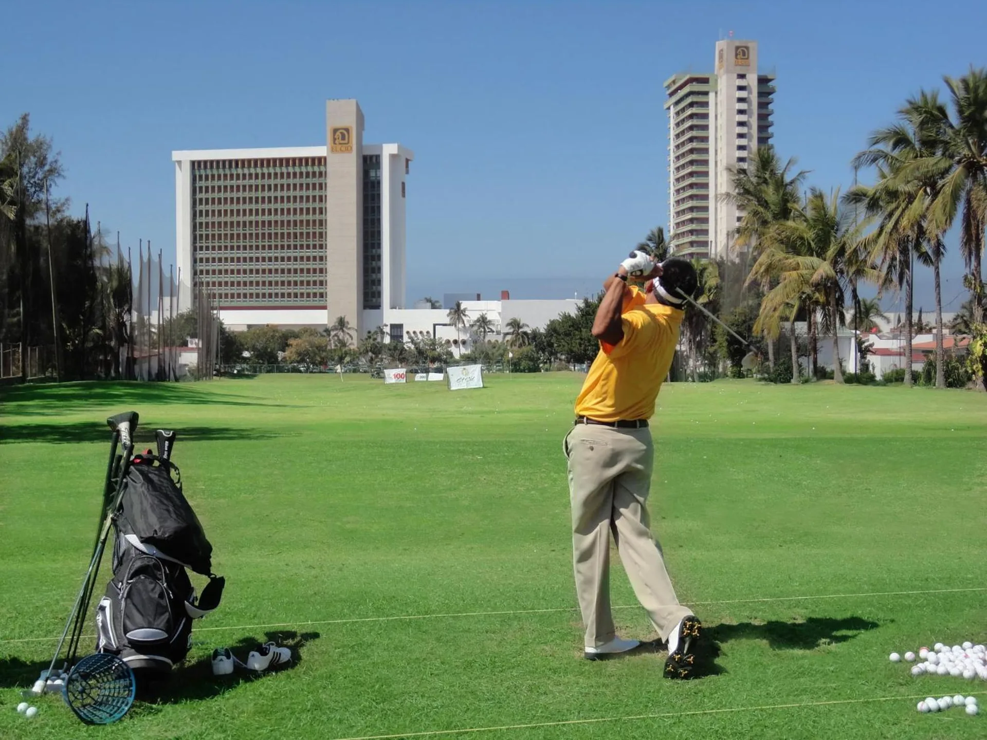 Golfer practicing on a green with hotel towers in the background at El Cid Granada Hotel.