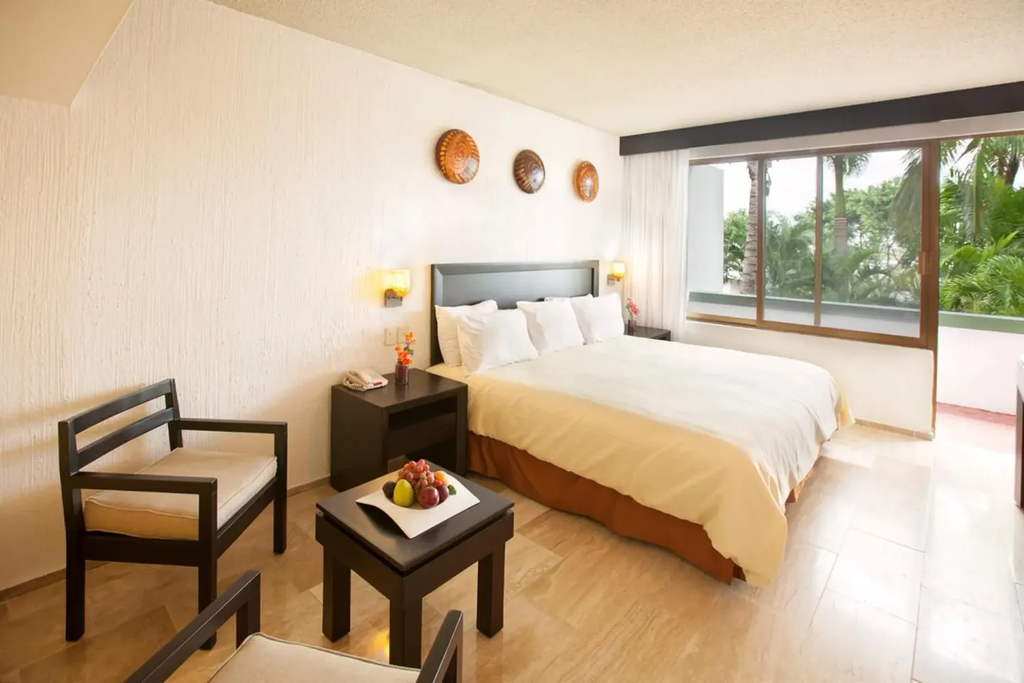 King bed guest room at El Cid Granada Hotel with chairs, table, and balcony-side window.