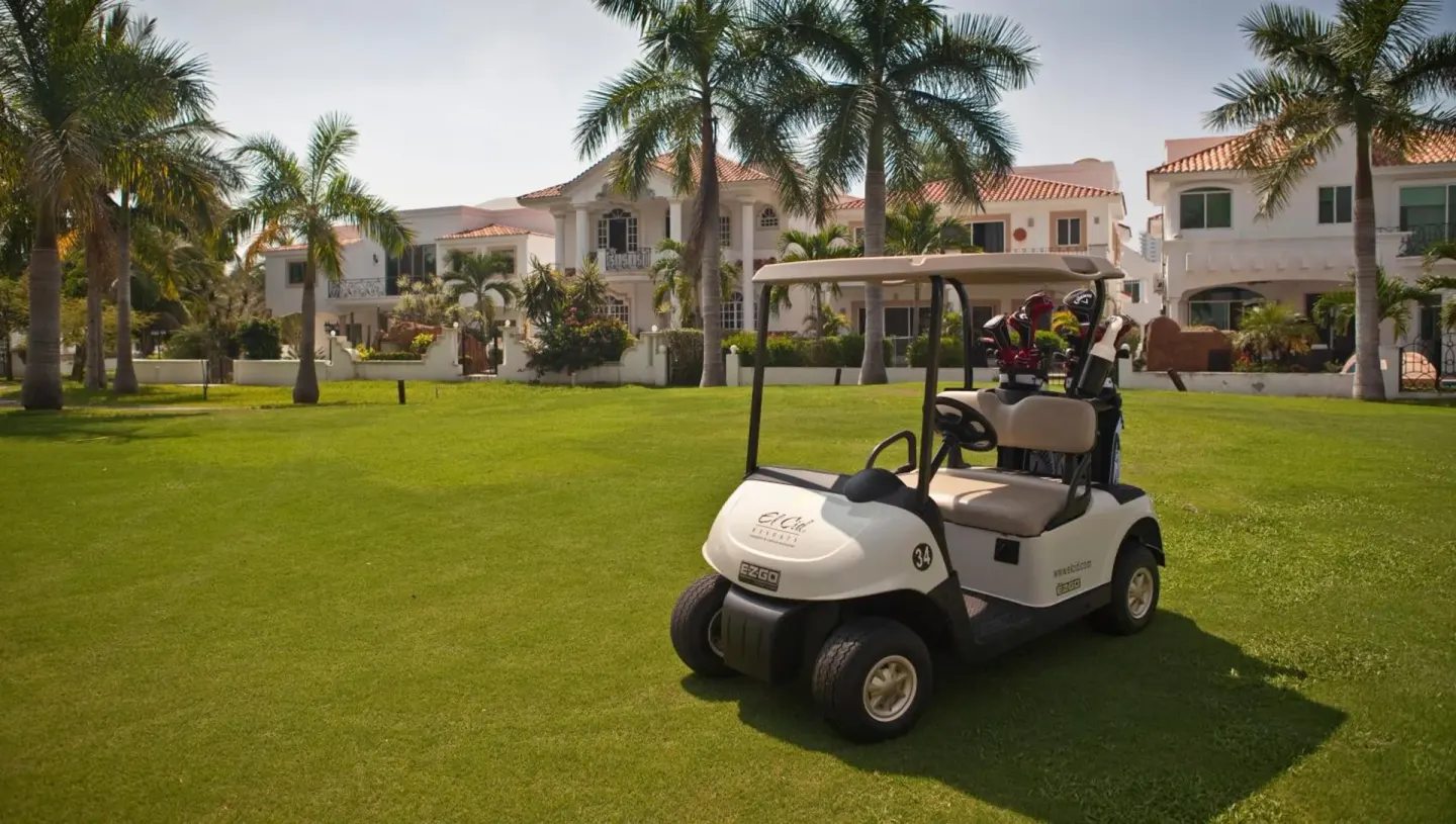 Golf cart parked on a palm-lined lawn at El Cid Granada Hotel near white villas.