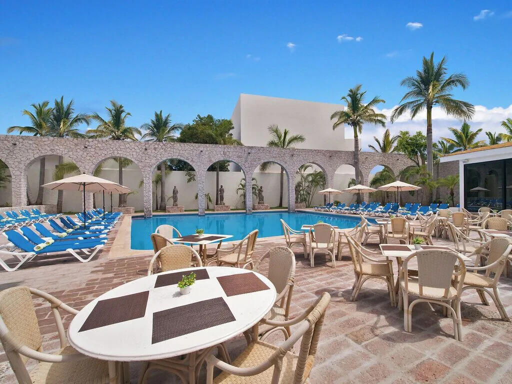 Poolside tables, loungers, palms and stone arches at El Cid Granada Hotel.