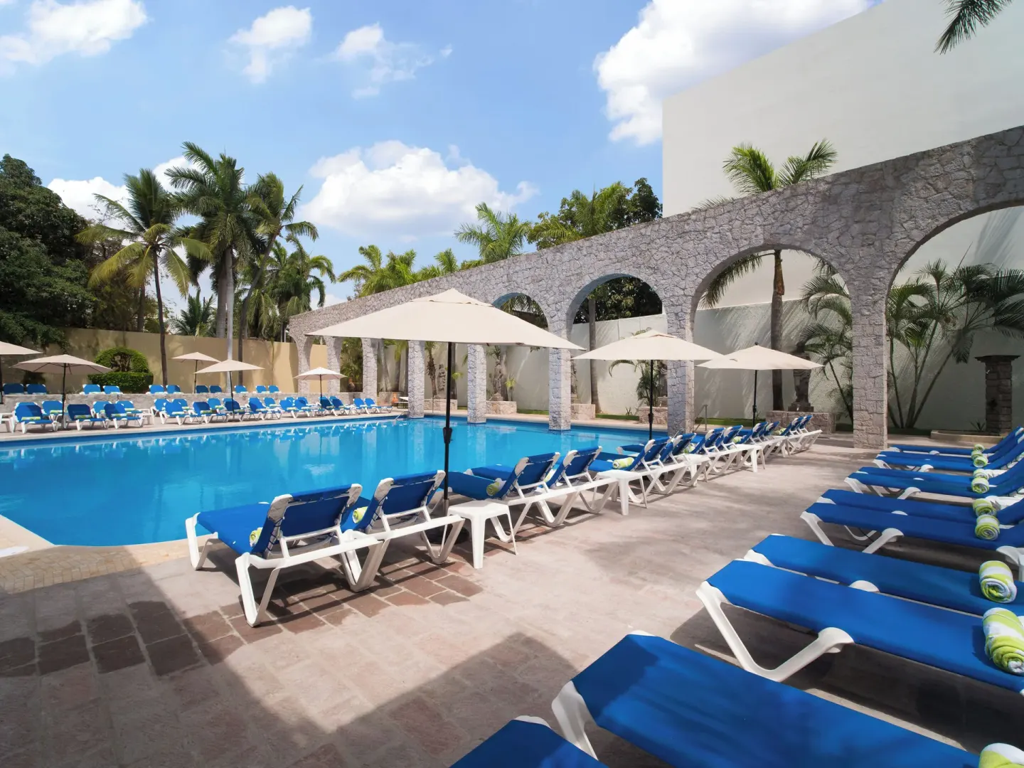 Resort pool lined with blue loungers and umbrellas at El Cid Granada Hotel.