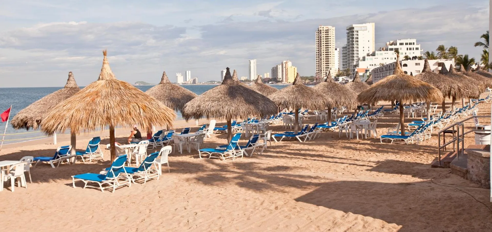 Beach palapas and blue lounge chairs at El Cid Marina Beach Hotel.