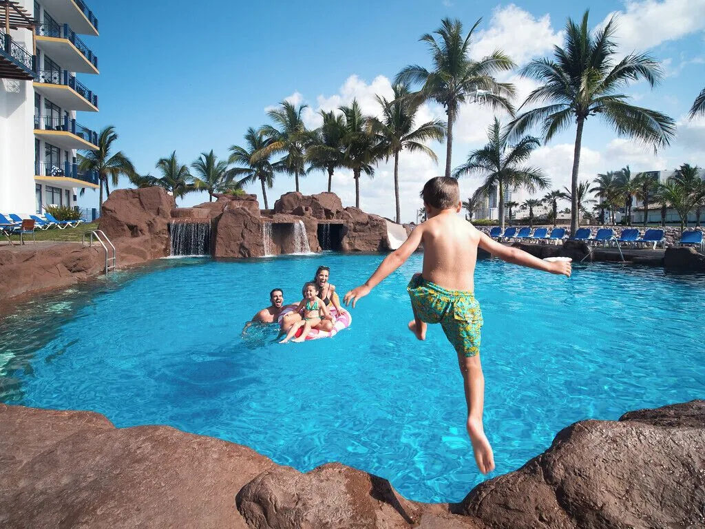 Child jumping into the pool with a family nearby at El Cid Marina Beach Hotel.