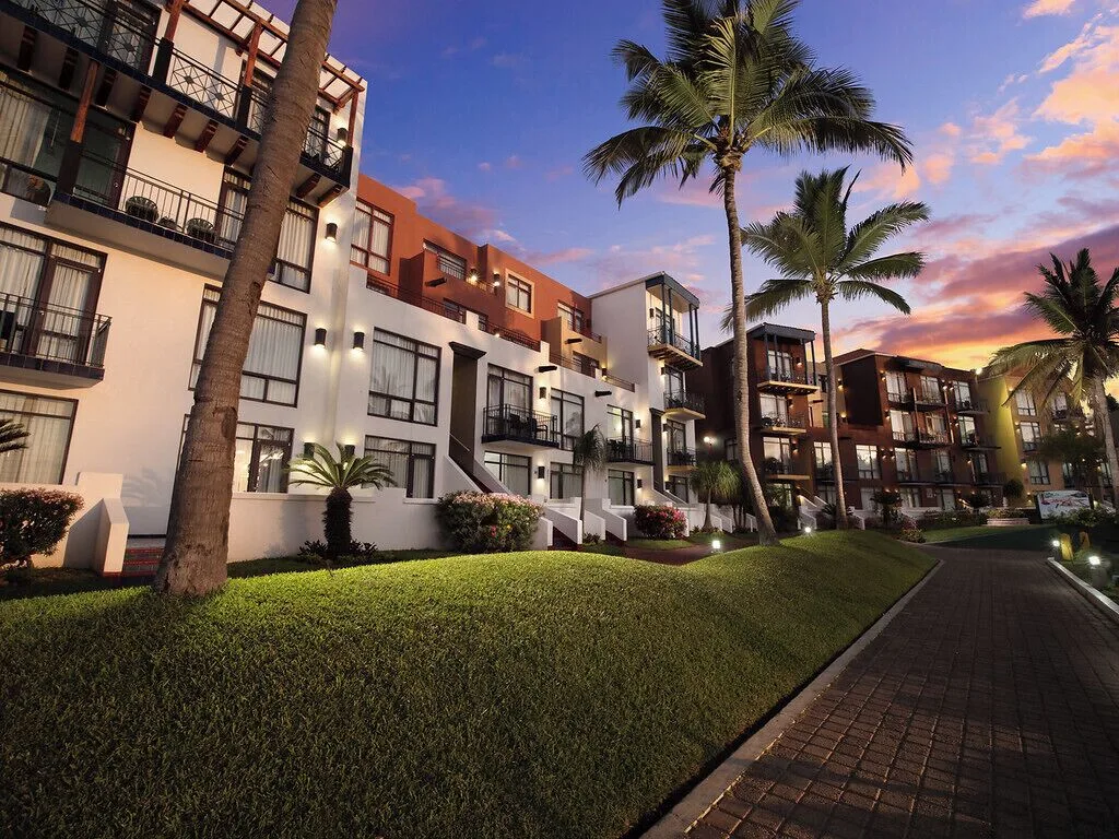 Guest buildings and palm-lined walkway at dusk at El Cid Marina Beach Hotel.