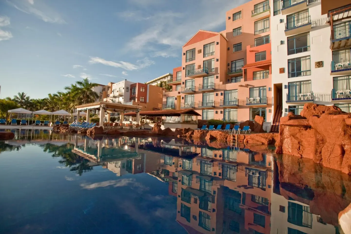 Pool reflecting guest buildings and red rock features at El Cid Marina Beach Hotel.