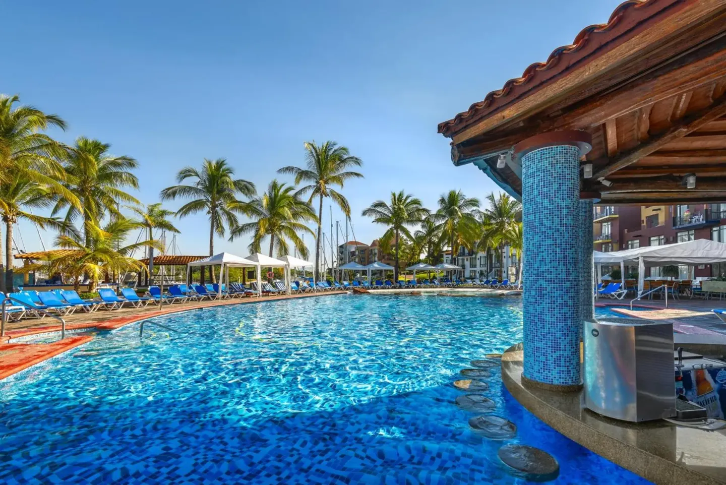 Swimming pool with lounge chairs and palm trees at El Cid Marina Beach Hotel.