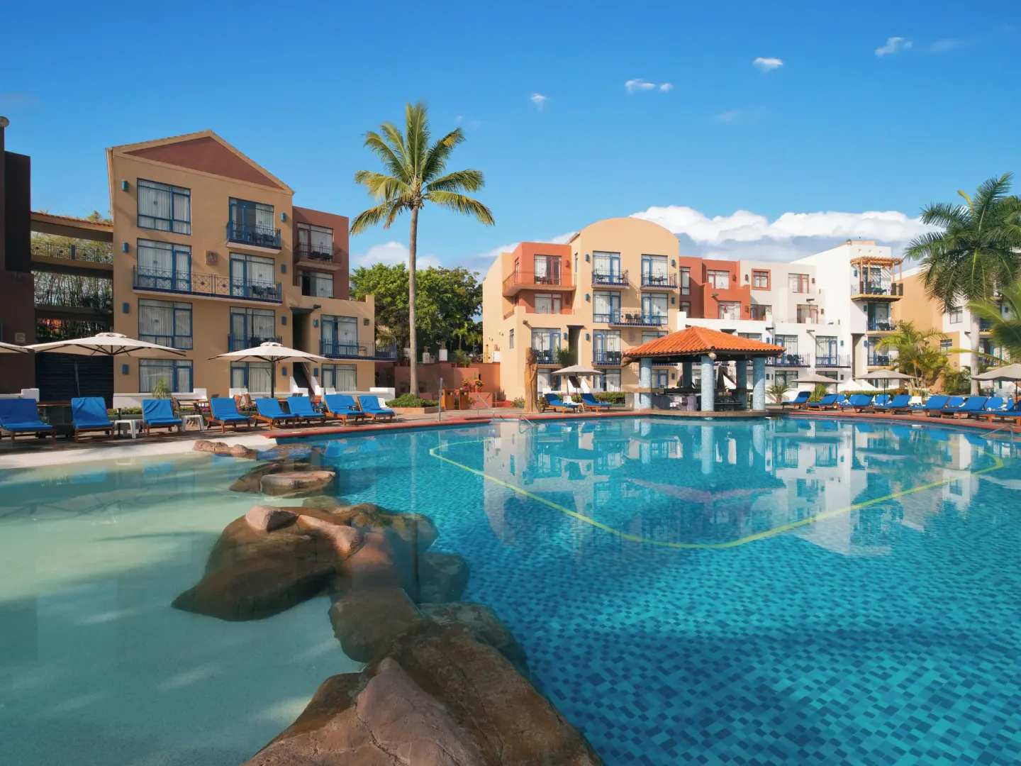Resort pool with lounge chairs and colorful buildings at El Cid Marina Beach Hotel.